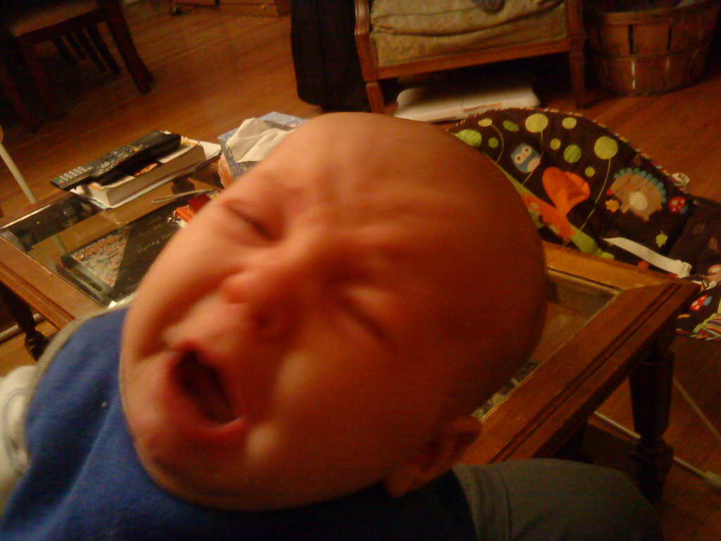 Infant screaming with Fisher Price baby bouncer seat in background