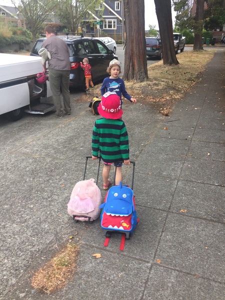 Child pulling two kid suitcases, a pink fuzzy one from Popatu and a blue shark one from Yodo
