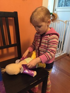 Preschooler child changing clothes on Baby Stella doll by Manhattan Toy