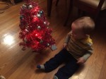 Baby in fleece pants sitting next to small pink Christmas tree