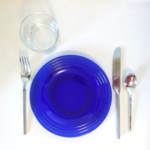 Blue glass plate with silverware and clear glass plate setting