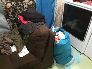 Piles of laundry in bags, on chaise lounge, and in basket shown next to dryer