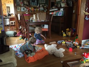 Dining room shown covered in stuff with toys scattered over floor with two kids playing