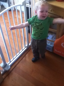 Crying toddler holding onto the First Years Hands free baby gate