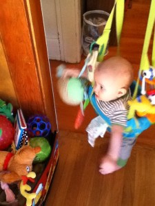 Infant playing in Johnny Jump Up doorway jumper near a bin of toys