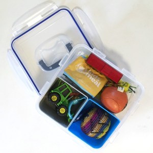 Clear square container packed with small toys for long car ride