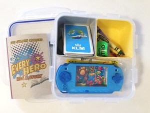 Busy box for kids with deck of cards, crayons, small notebook, slap bracelet, and handheld game inside compartments