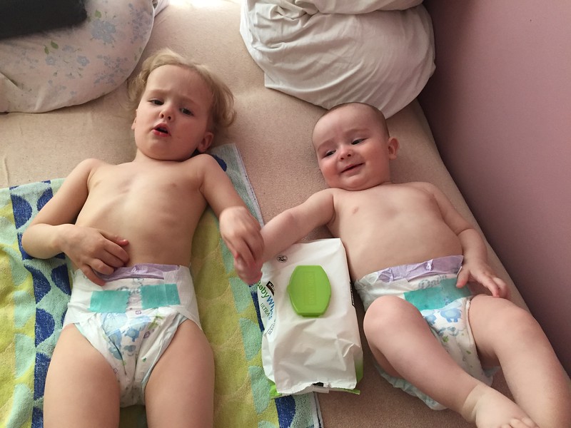 Toddler and infant lying on bed on towel wearing diapers holding hands