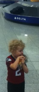 Toddler wearing football jersey in front of baggage claim at airport