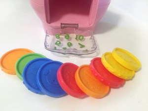 Plastic large coins in orange, green, blue, red, and yellow laid out in front of open door on fisher price laugh and learn piggy bank