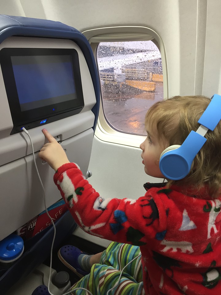 Preschooler wearing blue kids headphones on board airplane adjusting seatback screen entertainment