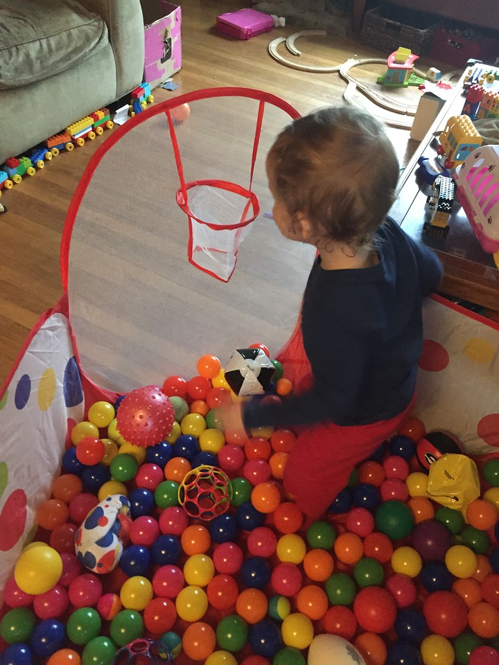 Toddler in pop up ball pit filled with balls with basketball hoop