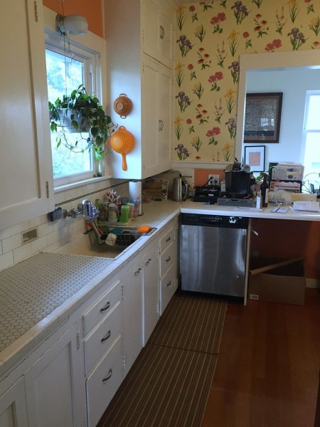 Kitchen with white cabinets and flowered wallpaper hanging plant and tile countertops