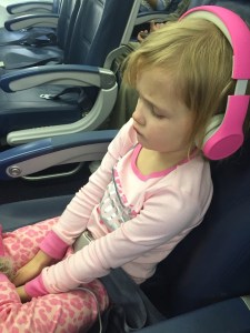Child dressed in pink wearing pink kids headphones onboard airplane