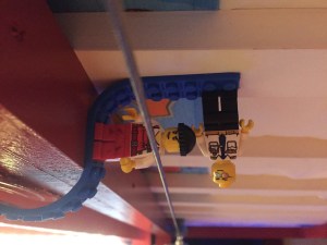 Lego minifigs stuck sideways and hanging upside down from Mayka toy brick block tape in blue underneath bunk bed