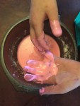 Pink gloop covering child's hands over bowl
