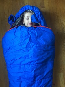 Child inside REI Nodder kids sleeping bag in blue with red zipper accents