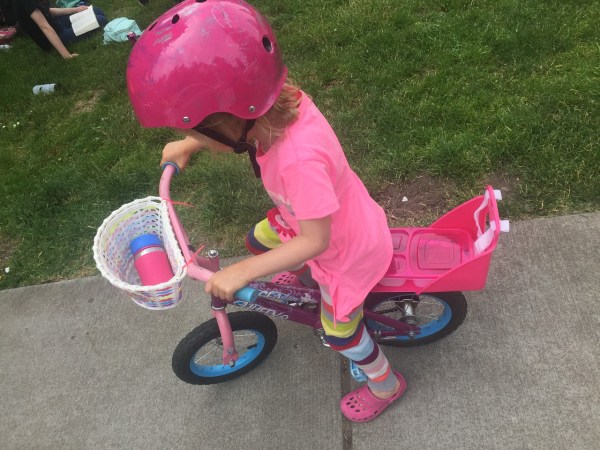 Preschooler on 12 inch wheel bike with baby doll seat attached in rear