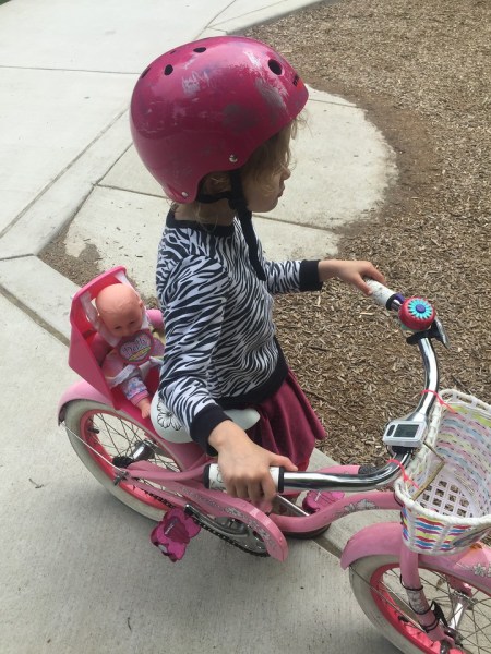 child riding bike with baby strapped into seat over back wheel
