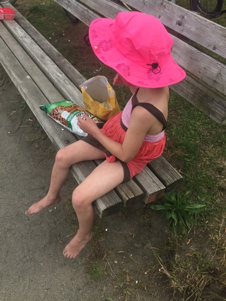 Girl wearing pink sun hat eating snacks on beach