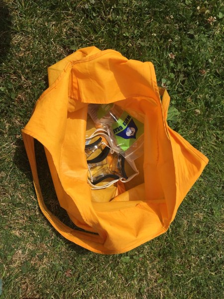 Yellow waterproof bag shown open with goggles inside on grass
