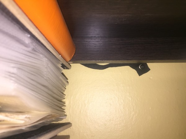 Furniture anchor partially visible underneath shelf next to stack of books