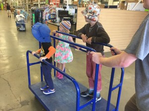 Three kids riding on blue flat car in home improvement store
