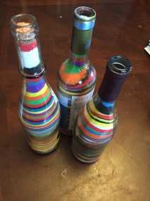 Three wine bottles filled with layers of different colored sand by young children