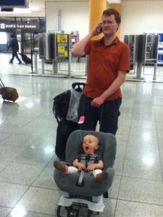 Infant riding in car seat on wheeled travel cart Britax through airport