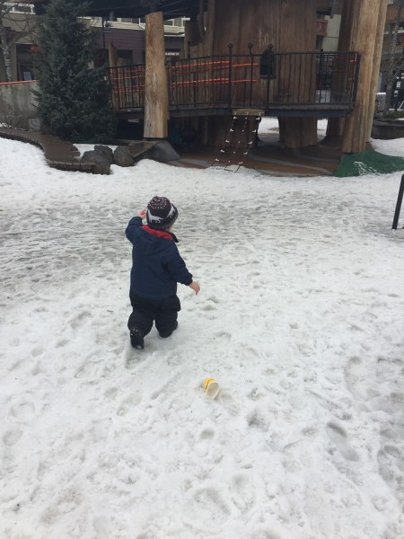 Child in snow clothes and boots walking through snow to playground
