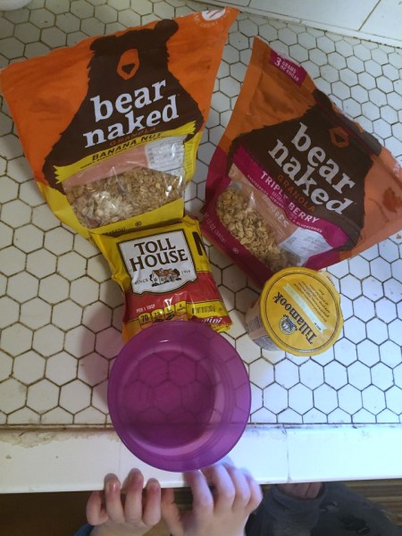 Empty bowl on counter with small child hands, tollhouse chocolate chips, and bear naked granola, tillamook yogurt