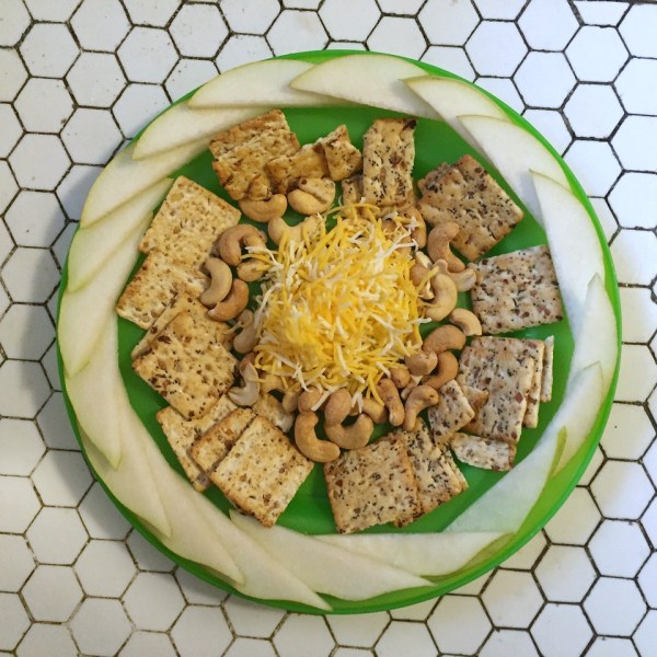 Kids snacks of sliced pears, crackers, cashews, and shredded cheese arranged on bright green plate