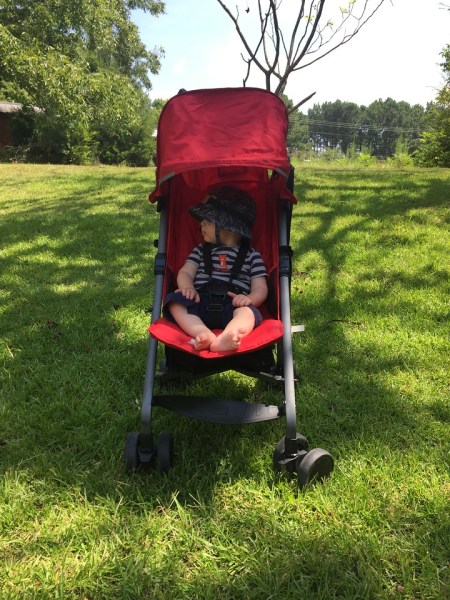 Infant riding in red Joovy Ultralight umbrella stroller parked on the grass