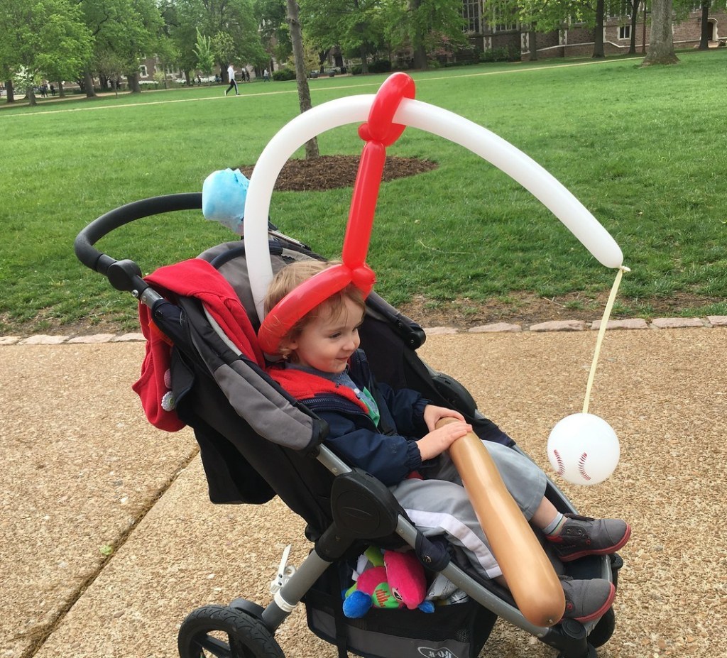 Two and a half year old child riding in BOB motiong stroller with balloon baseball bat and baseball to swing at