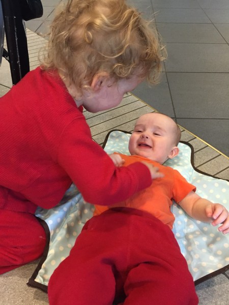 Infant laying on Skip Hop Pronto diaper changing station getting tickled by older sibling