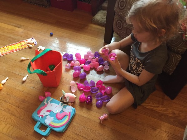Child with pink and purple plastic Easter eggs opened in pile on floor