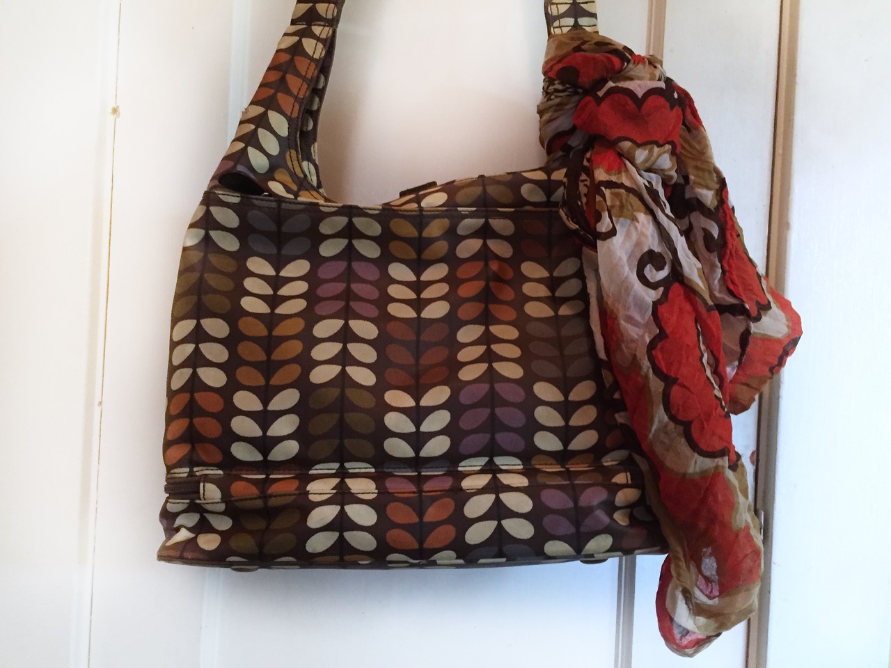 Orla Kiely diaper changing bag with multicolor infinity scarf tied to handle hanging on door