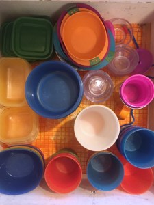 Kitchen drawer full of kid dishes cups bowls straws in bright colors and clear containers as seen from above