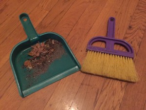 Schylling Little Helper dust pan and broom set with dirt and debris in green dustpan next to purple and yellow hand brush