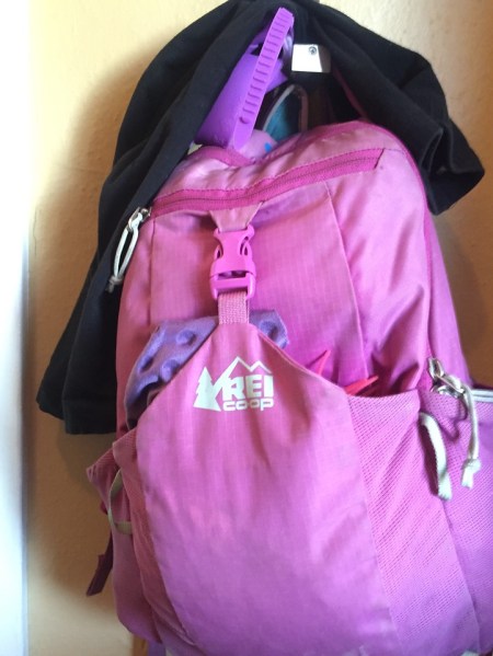Black leggings hanging on top of child's REI backpack for school
