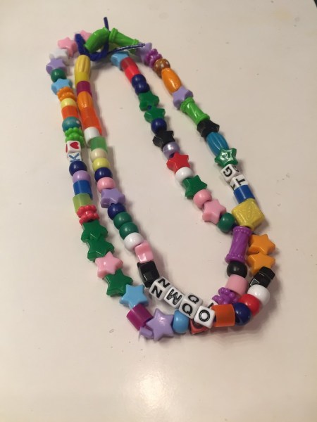 Bead necklace made by child in colored plastic beads on ribbon