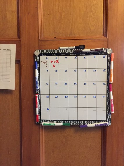 Dry erase magnetic monthly calendar board on wood paneled wall