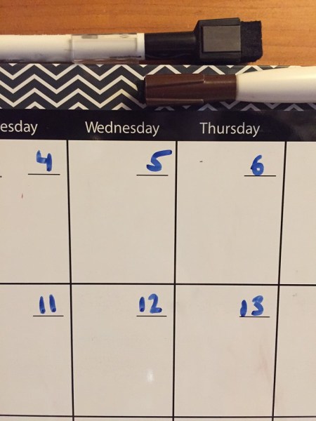 Close up of dry erase calendar board and marker with dates numbers entered in boxes