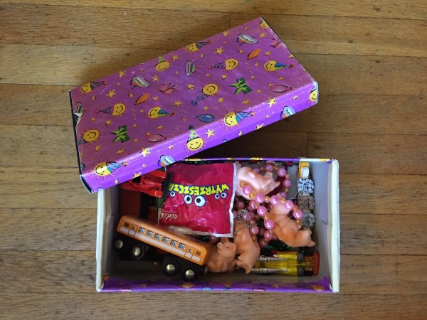 Shoe box with open lid covered in purple wrapping paper and filled with small toys as rewards for kids