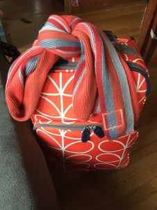 Orla Kiely orange flower print roller board suitcase with knitted striped scarf tied to handle