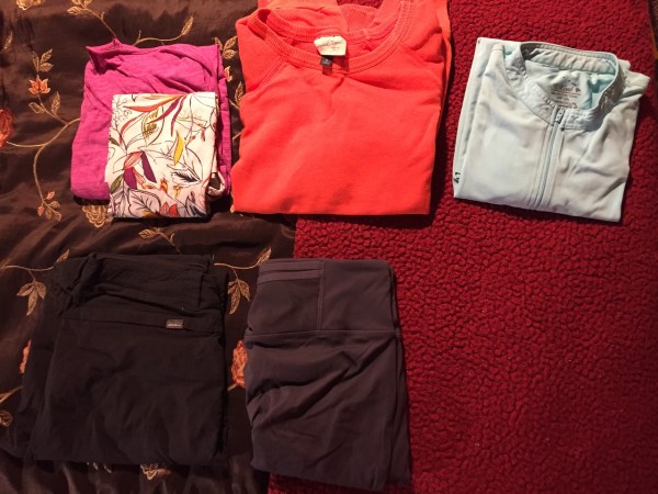 Clothes folded and laid out on bed in preparation for packing