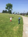Two kids running through grass at a park on a sunny day with blue skies
