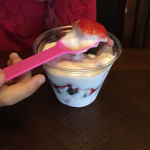 Child eating strawberries and blueberries mixed with yogurt