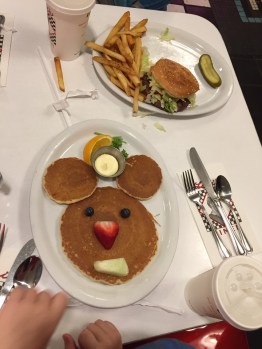 Pancakes arranged into mouse head shape with berry eyes and fruit nose and mouth