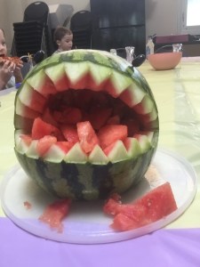 Shark shaped watermelon holding watermelon chunks on table at child's birthday pool party